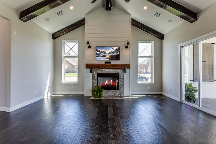 Spacious living room with vaulted ceiling, fireplace, mounted TV, large windows, and hardwood flooring.