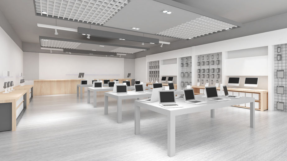 Modern electronics store interior with laptops on tables, minimalist design, and displays on walls.